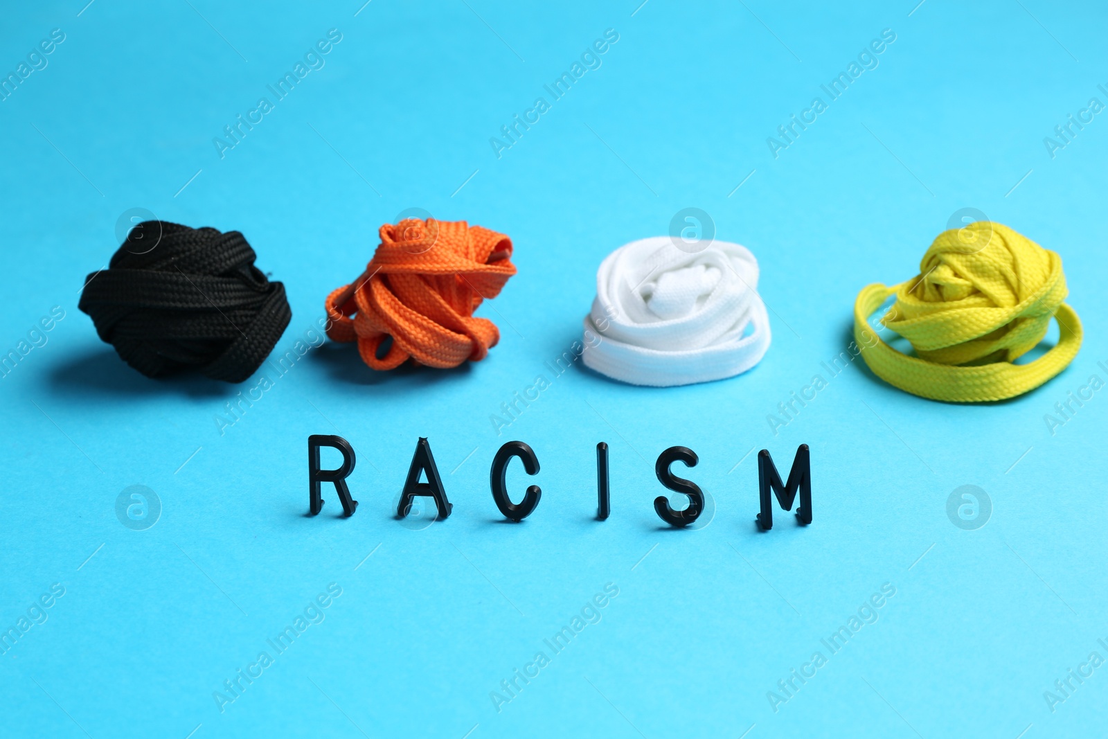 Photo of Word Racism and shoelaces of different colors on light blue background