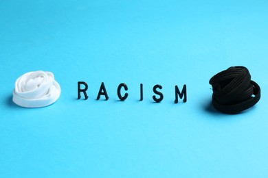 Photo of Word Racism and shoelaces of different colors on light blue background