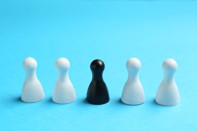 Photo of Stop racism. One black human figure among white ones on light blue background, closeup