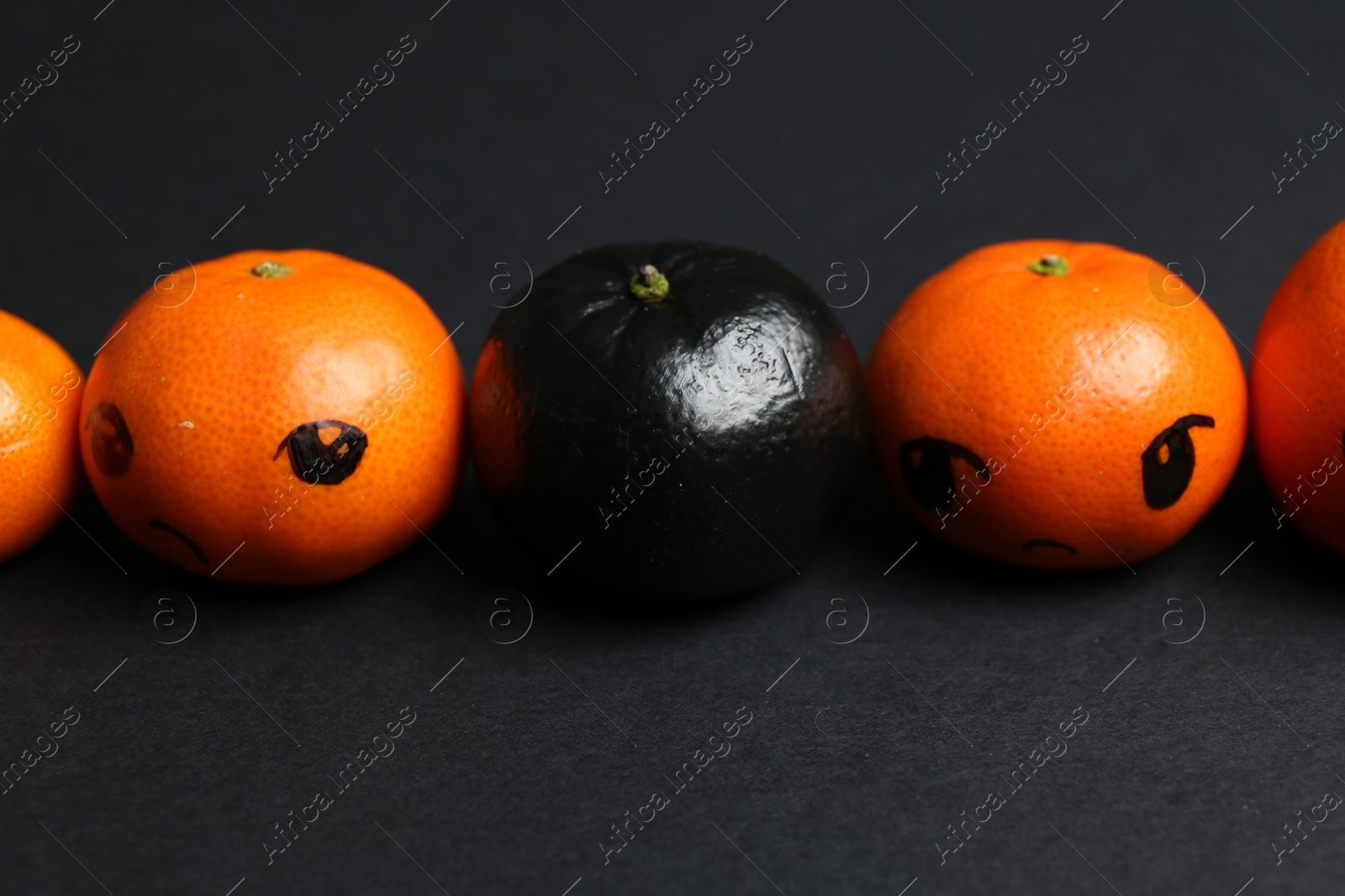 Photo of Stop racism. One black tangerine among orange ones on black background, closeup