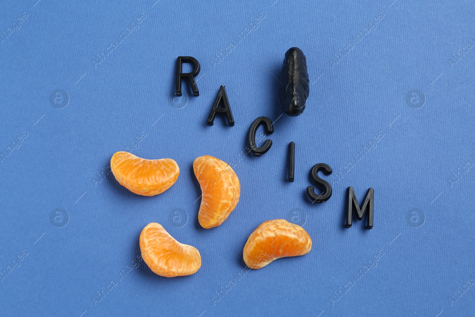 Photo of Word Racism and tangerine segments of different colors on blue background, flat lay