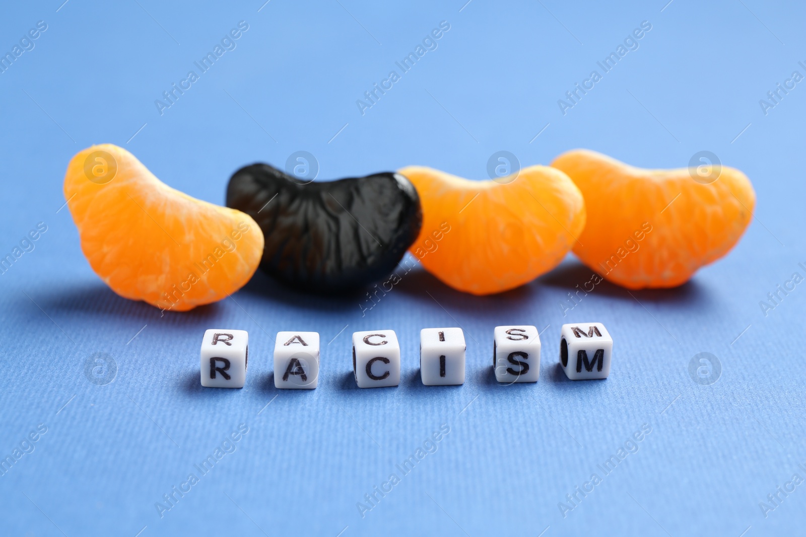 Photo of Word Racism and tangerine segments of different colors on blue background, closeup