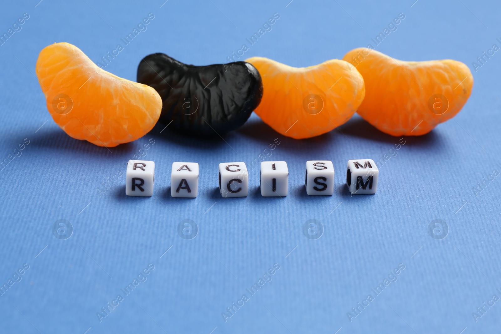 Photo of Word Racism and tangerine segments of different colors on blue background, closeup