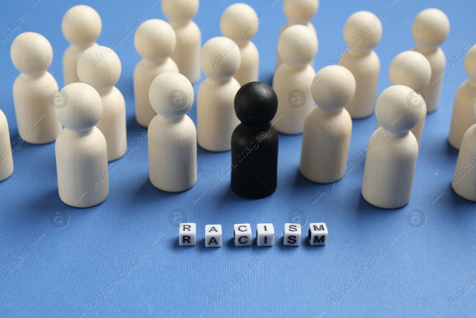 Photo of Word Racism and human figures of different colors on blue background, closeup