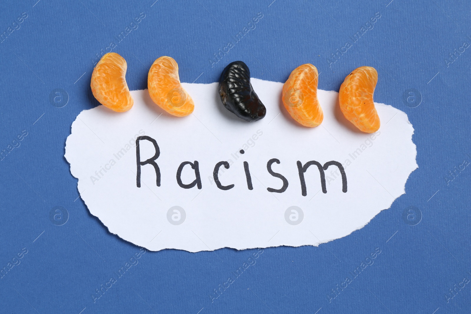 Photo of Card with word Racism and tangerine segments of different colors on blue background, top view