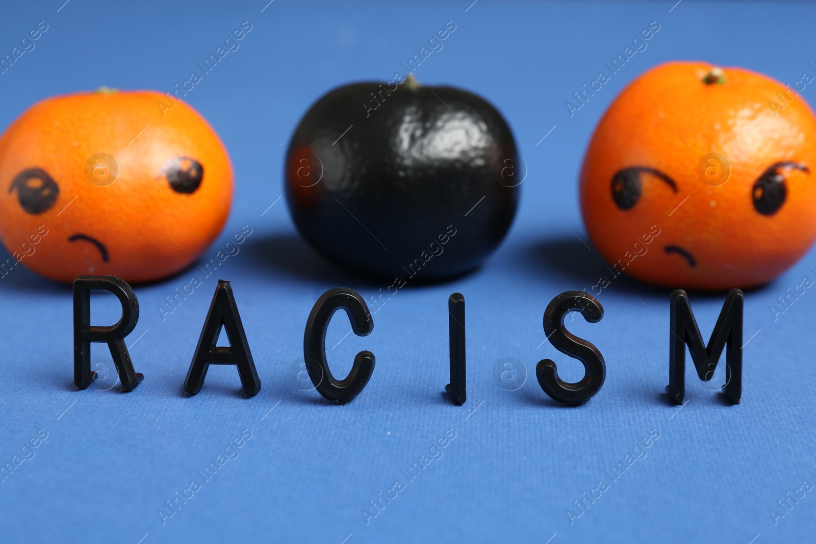 Photo of One black tangerine among orange ones and word Racism made with beads on blue background, closeup