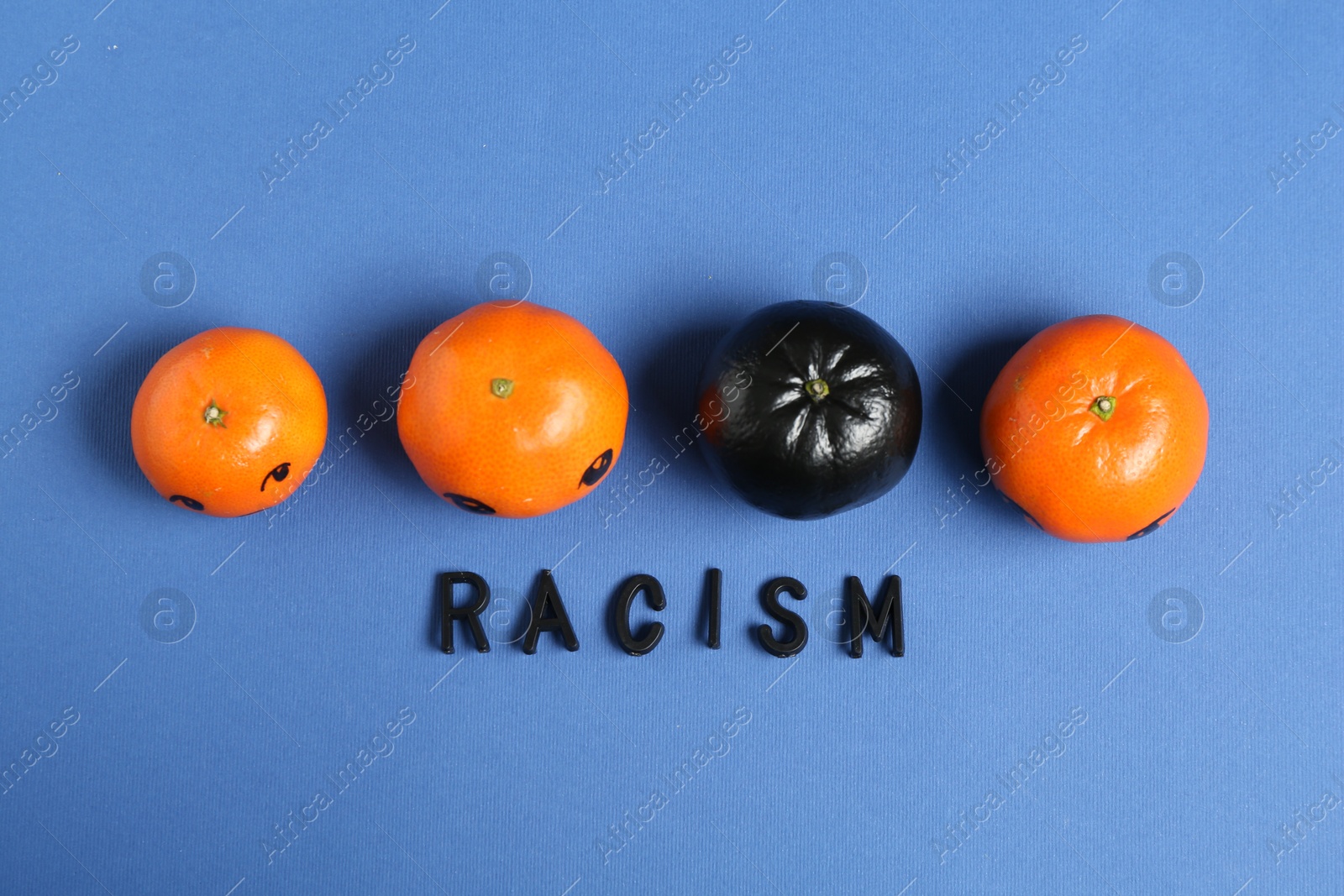 Photo of One black tangerine among orange ones and word Racism made with beads on blue background, top view