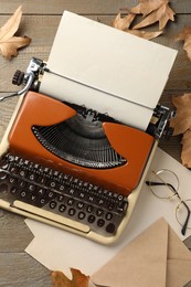 Vintage typewriter with paper sheet, envelope, glasses and leaves on wooden table, flat lay