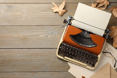Photo of Vintage typewriter with paper sheet, envelope, glasses and leaves on wooden table, flat lay. Space for text