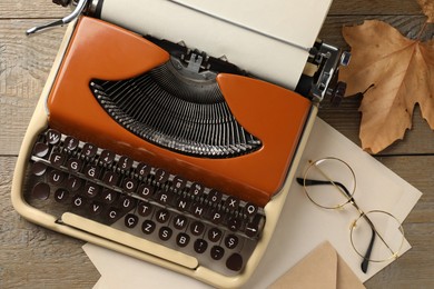 Photo of Vintage typewriter with paper sheet, envelope, glasses and leaves on wooden table, flat lay