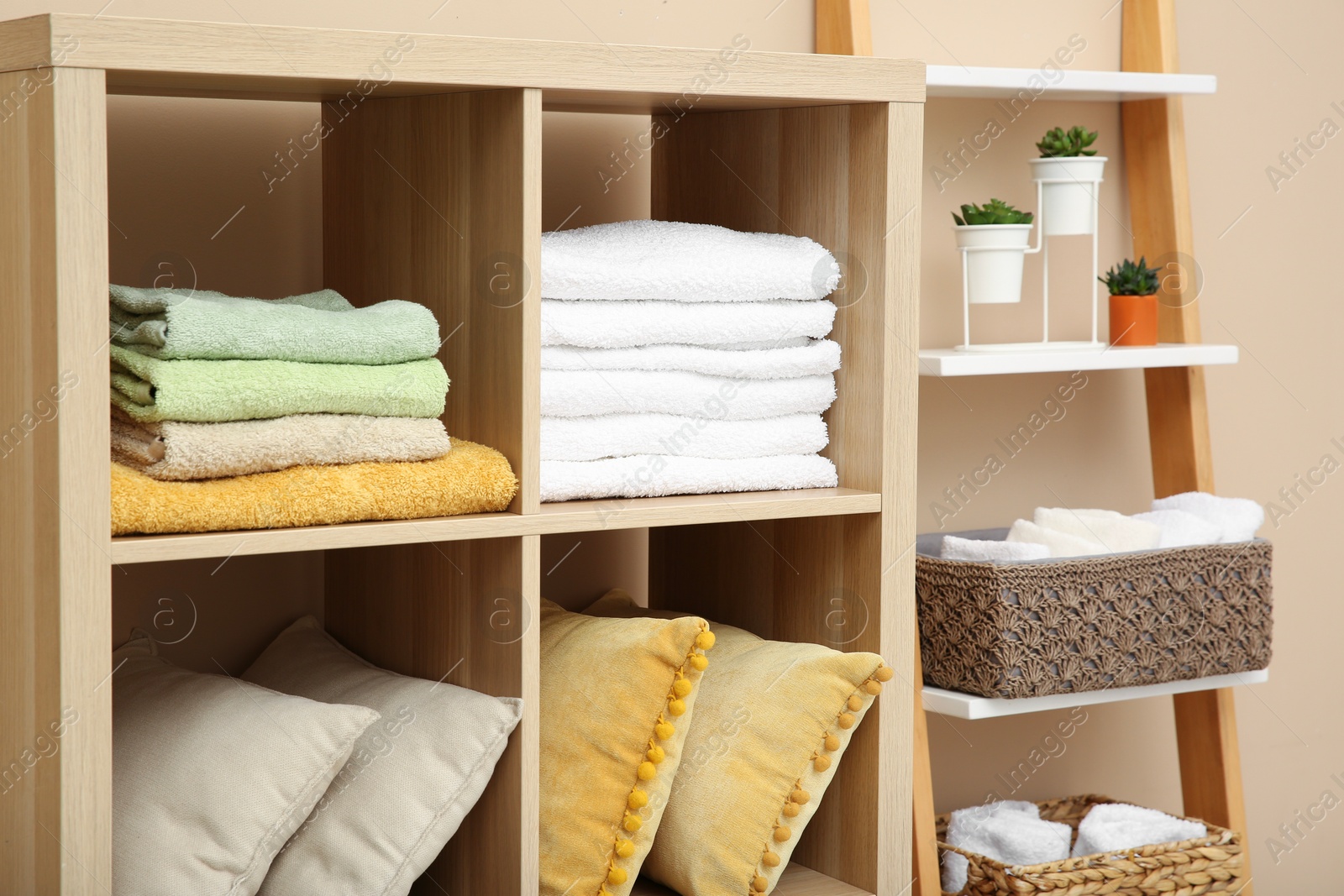 Photo of Folded towels and pillows on shelving unit indoors. Home textile storage