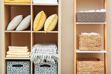 Photo of Folded linens and pillows on shelving unit indoors. Home textile storage