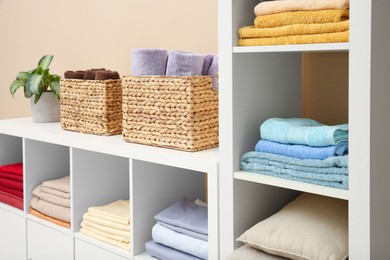 Photo of Folded linens, towels and pillows on shelving unit indoors. Home textile storage