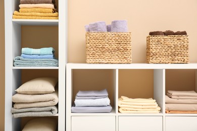 Photo of Folded linens, towels and pillow on shelving unit indoors. Home textile storage