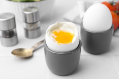 Photo of Soft boiled eggs in cups served on white table, closeup