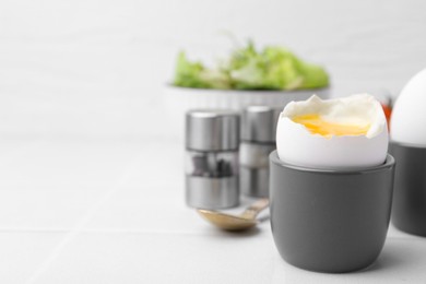 Soft boiled eggs in cups served on white tiled table, closeup. Space for text