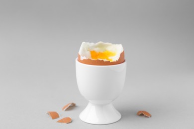 Soft boiled egg in cup and eggshell on light grey background