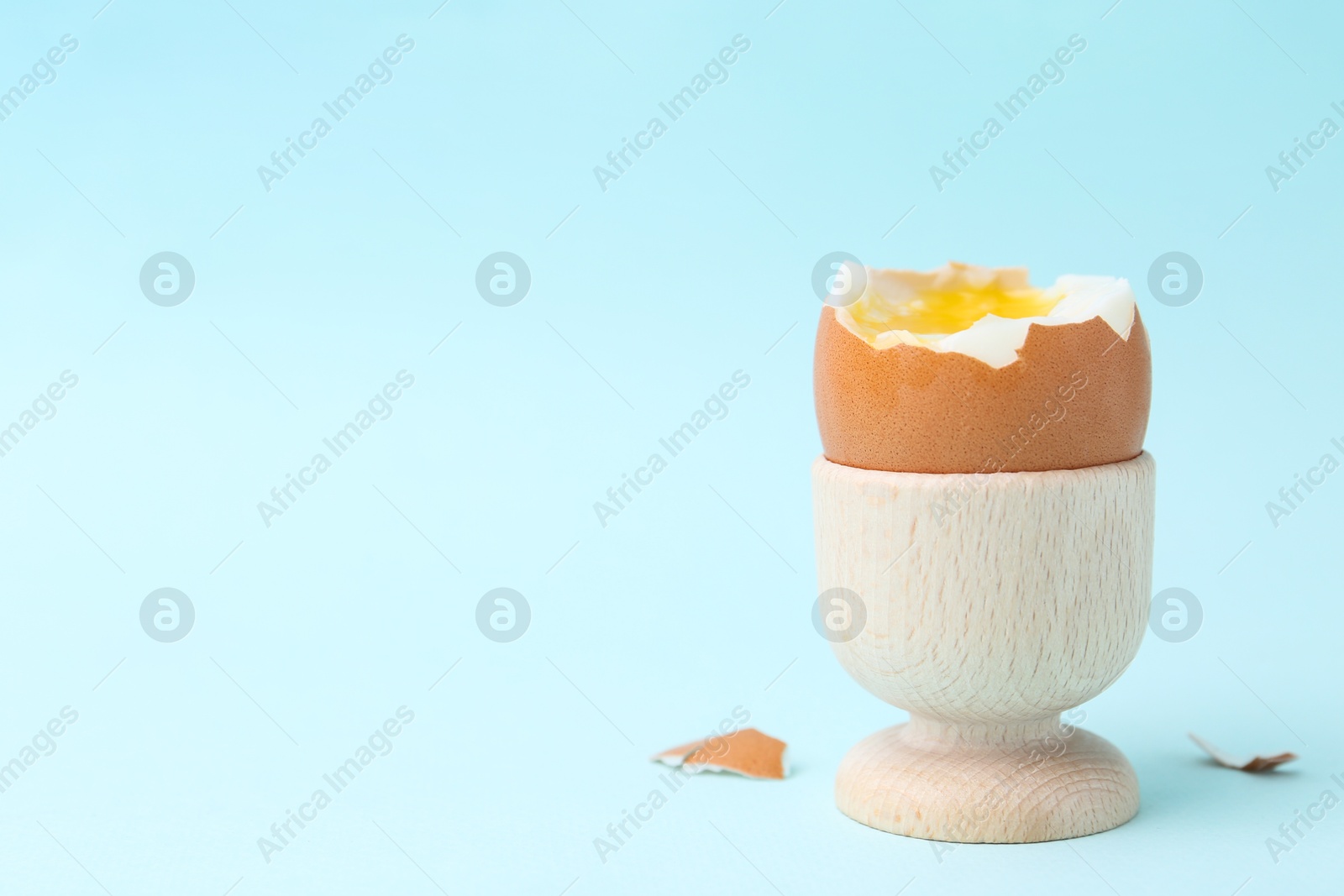 Photo of Soft boiled egg in eggcup on light blue background, closeup. Space for text