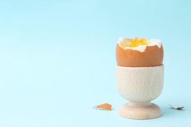 Photo of Soft boiled egg in eggcup on light blue background, closeup. Space for text