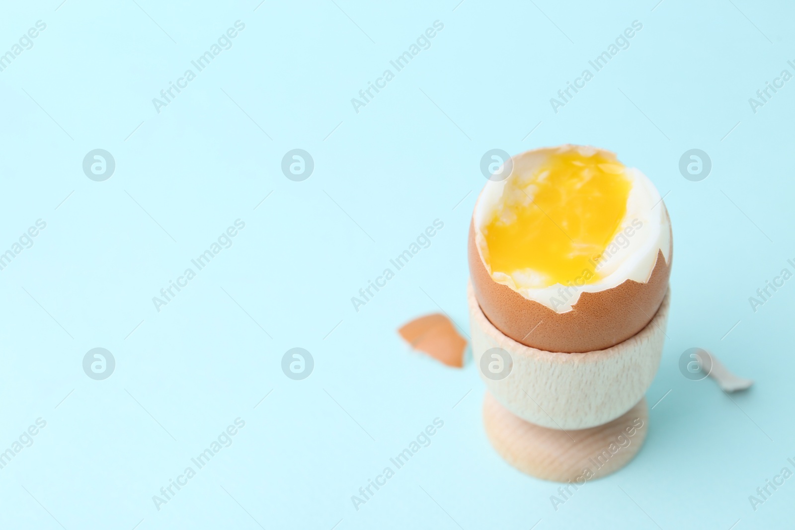 Photo of Soft boiled egg in eggcup on light blue background, closeup. Space for text