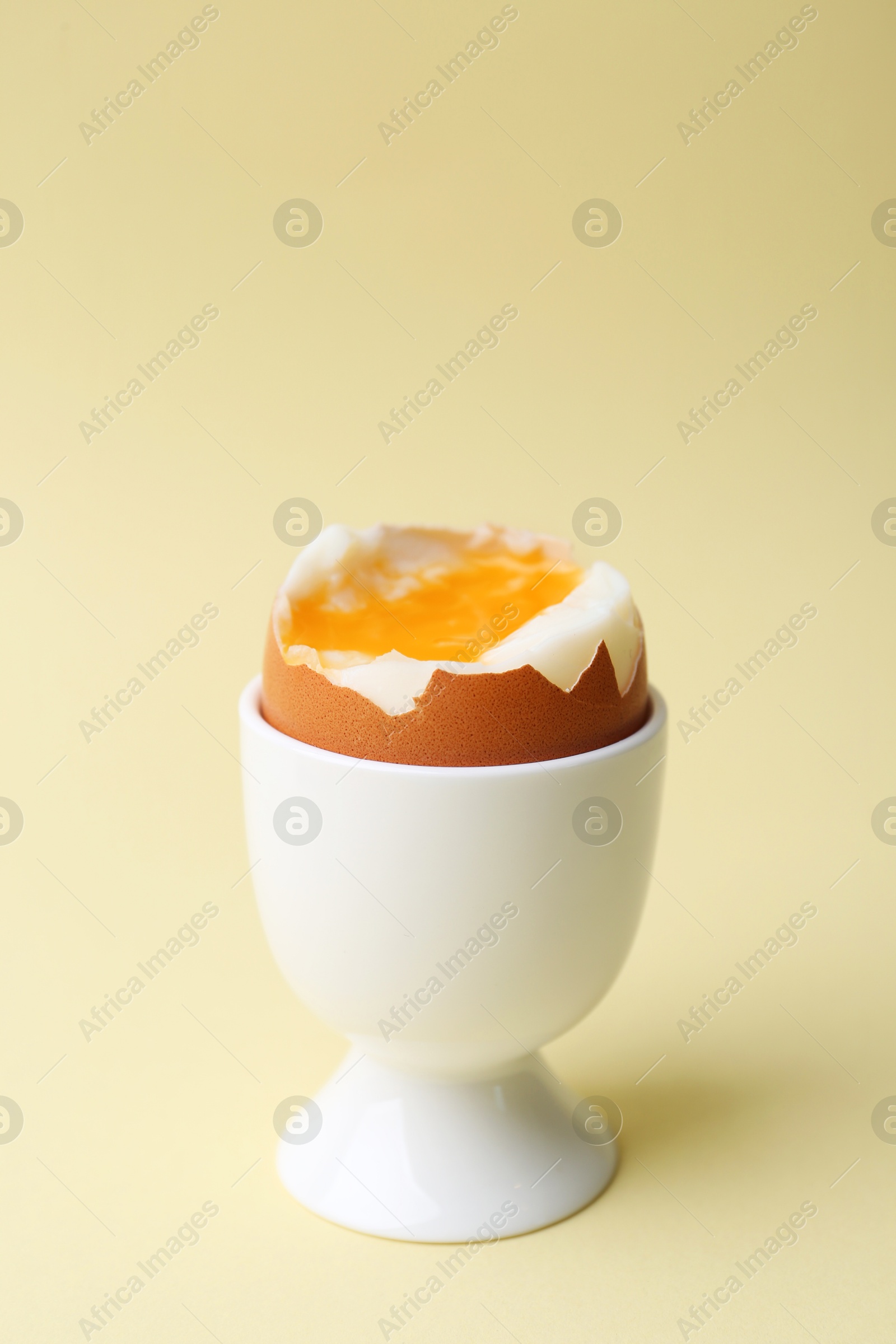 Photo of Soft boiled egg in eggcup on beige background, closeup