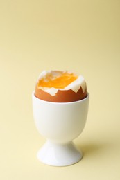 Photo of Soft boiled egg in eggcup on beige background, closeup