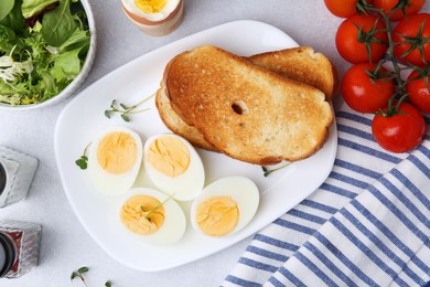 Photo of Hard boiled eggs with bread and tomatoes on light table, flat lay