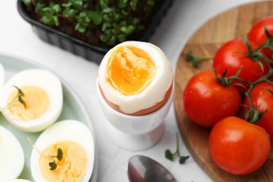 Photo of Boiled eggs, tomatoes and microgreens on white tiled table, closeup