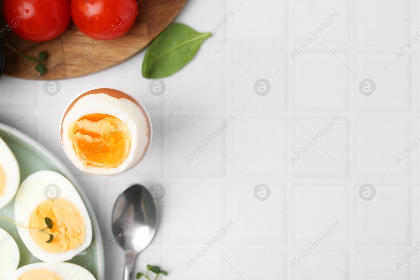 Photo of Boiled eggs and tomatoes on white tiled table, flat lay. Space for text