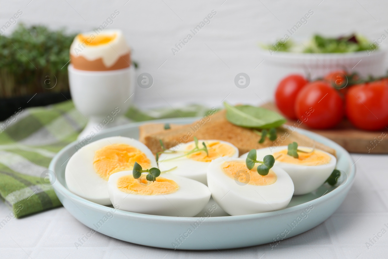 Photo of Cut hard boiled eggs with bread on white tiled table, closeup