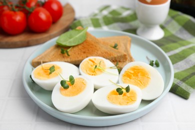 Photo of Cut hard boiled eggs with bread on white tiled table, closeup