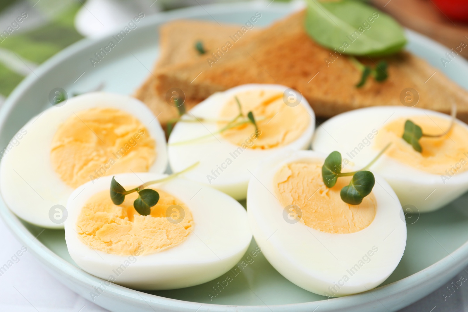 Photo of Cut hard boiled eggs with bread on white tiled table, closeup