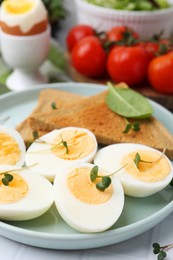 Photo of Cut hard boiled eggs with bread on white tiled table, closeup