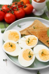 Photo of Cut hard boiled eggs with bread on white tiled table, closeup