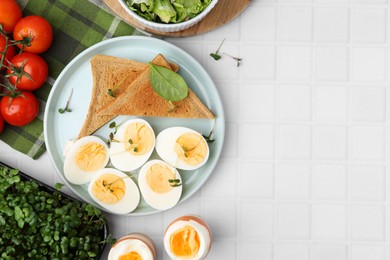 Photo of Cut hard boiled eggs with bread on white tiled table, flat lay. Space for text