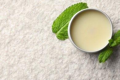 Photo of Mint lip balm and green leaves on beige textured background, top view. Space for text