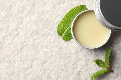 Photo of Mint lip balm and green leaves on beige textured background, top view. Space for text