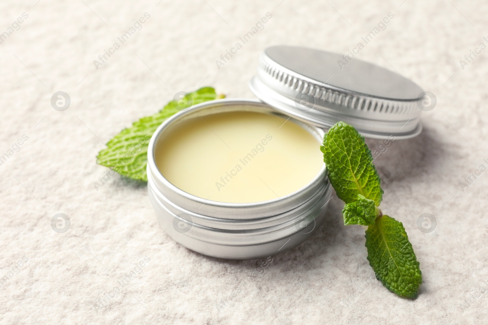 Photo of Mint lip balm and green leaves on beige textured table, closeup. Cosmetic product