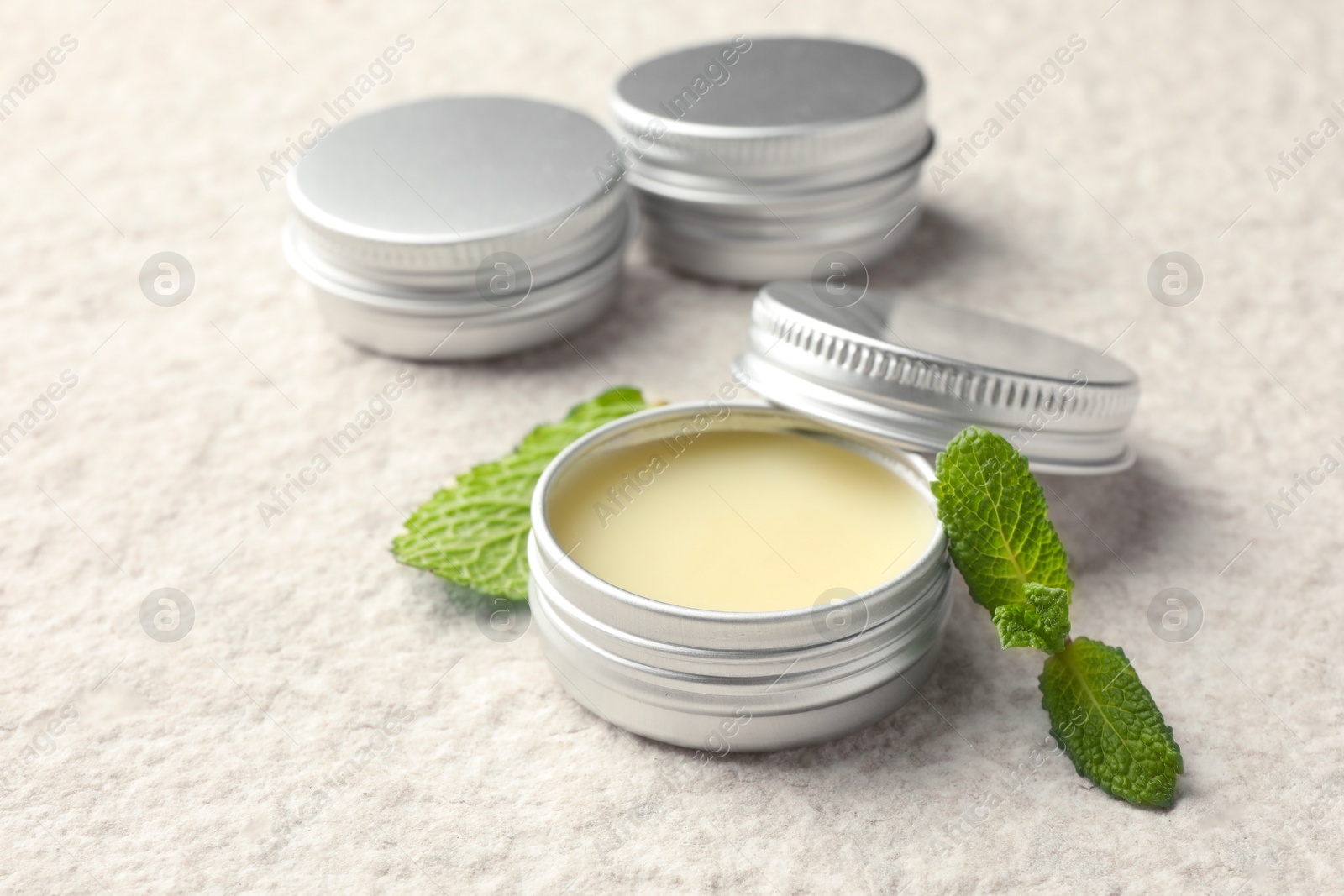 Photo of Mint lip balms and green leaves on beige textured table, closeup. Cosmetic product