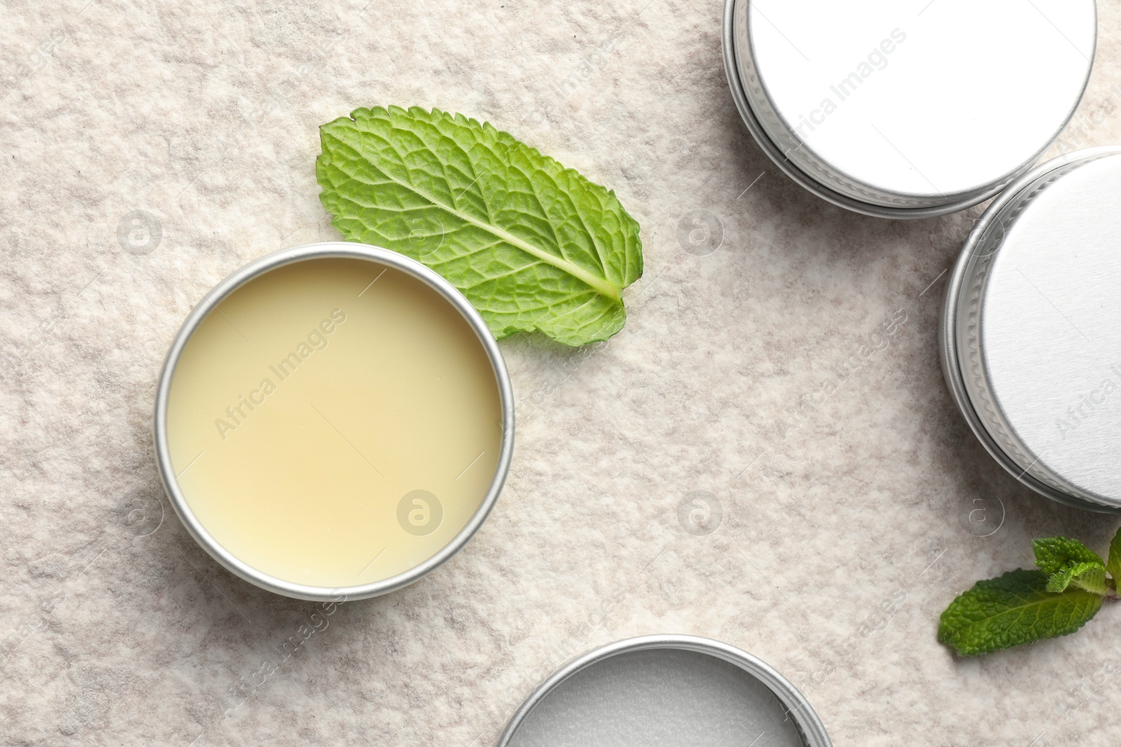 Photo of Mint lip balms and green leaves on beige textured background, flat lay. Cosmetic product