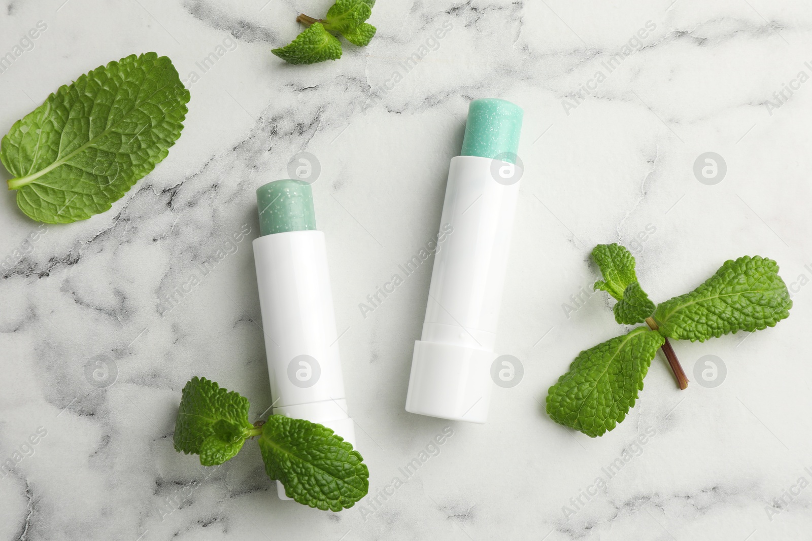 Photo of Natural lip balms and mint leaves on white marble background, flat lay