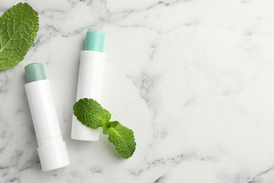 Photo of Natural lip balms and mint leaves on white marble background, flat lay. Space for text