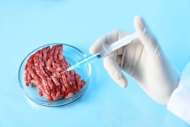 Photo of GMO concept. Scientist injecting something into minced meat at table in laboratory, closeup