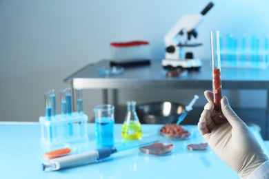 GMO concept. Scientist with meat in test tube at table, closeup. Space for text