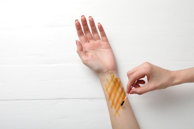 Photo of Woman applying topical iodine with cotton swab on hand at white wooden table, top view