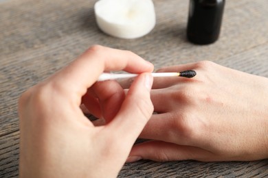 Photo of Woman applying topical iodine with cotton swab on hand at wooden table, closeup