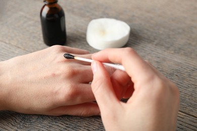 Photo of Woman applying topical iodine with cotton swab on hand at wooden table, closeup