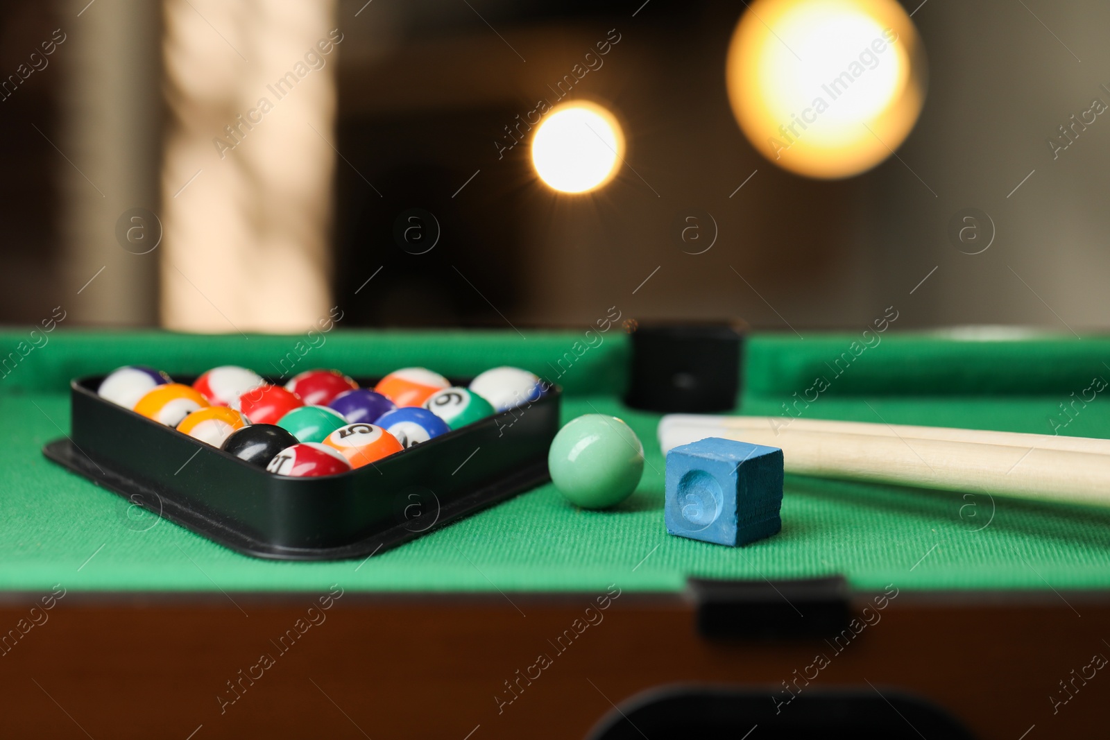 Photo of Many colorful billiard balls in triangle rack, cues and chalk on green table indoors, closeup