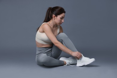 Photo of Woman in sportswear wearing sneakers on grey background