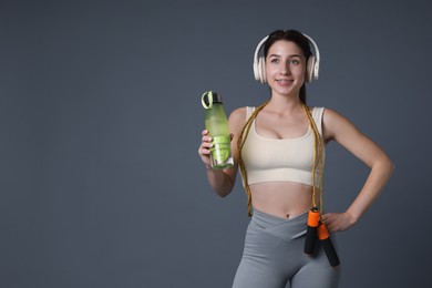 Photo of Woman in sportswear with headphones, bottle of water and skipping rope on grey background, space for text